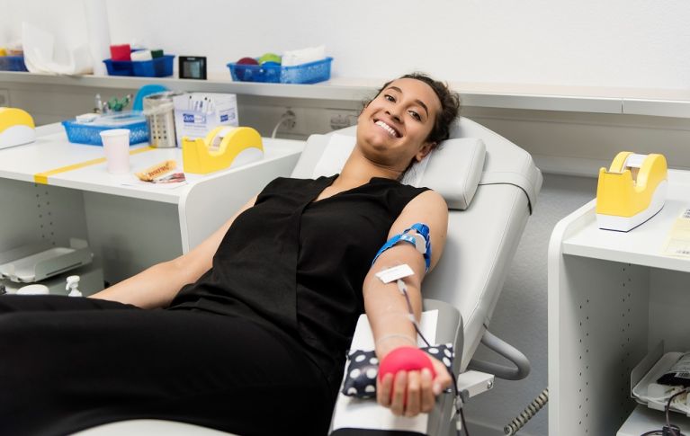 A young woman lies smiling on a stretcher and donates blood.