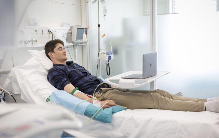 A young man undergoing peripheral blood stem cell donation. He is lying in a hospital bed, with intravenous lines visible on his arms.